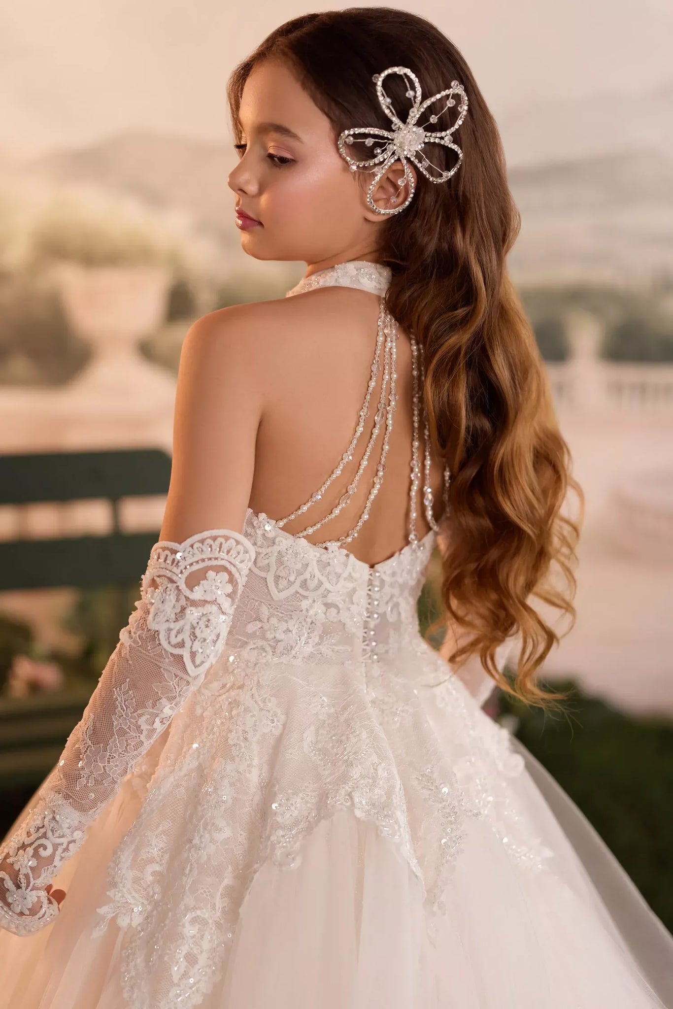 Girl wearing a white lace dress with pearl back detailing and a crystal hair accessory | Girls Formal Dress