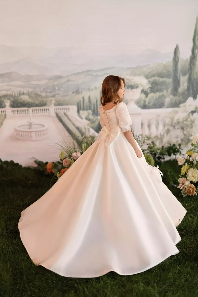 Girl wearing a ball gown with puff sleeves and a statement back bow standing on grass | Girls Formal Dress