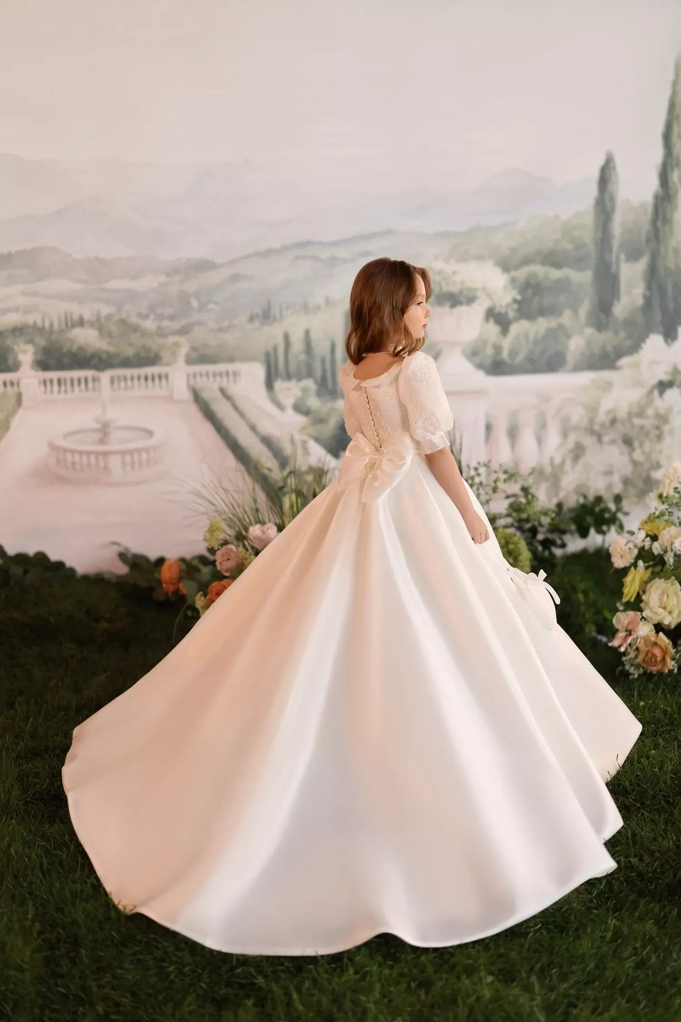 Girl wearing a ball gown with puff sleeves and a statement back bow standing on grass | Girls Formal Dress