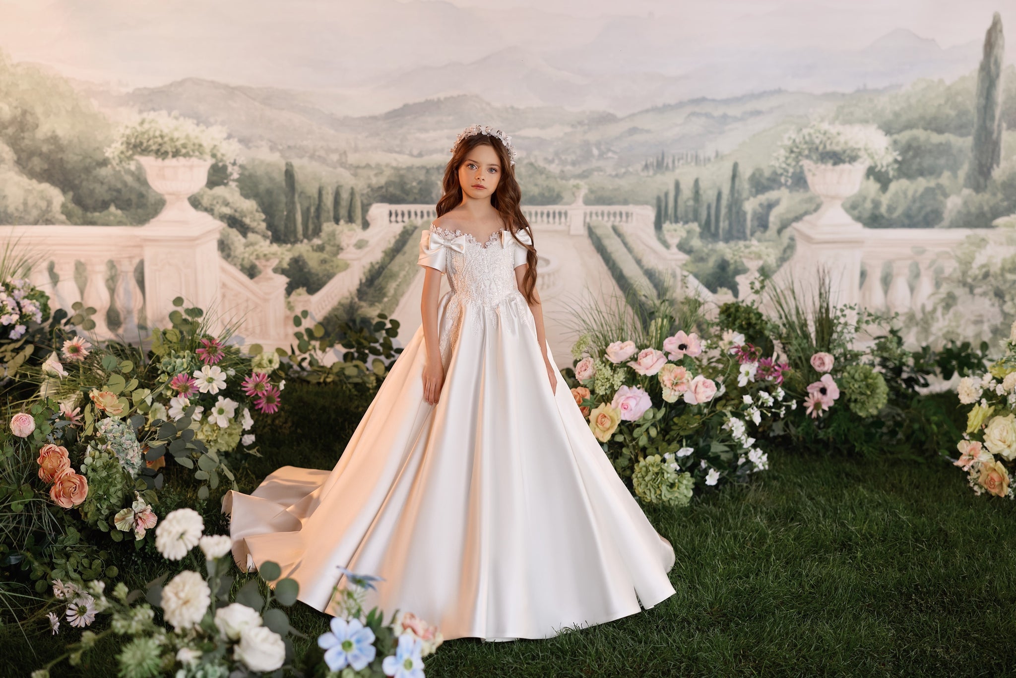 Girl wearing a white off the shoulder ball gown with lace bodice and floral headpiece in a garden setting