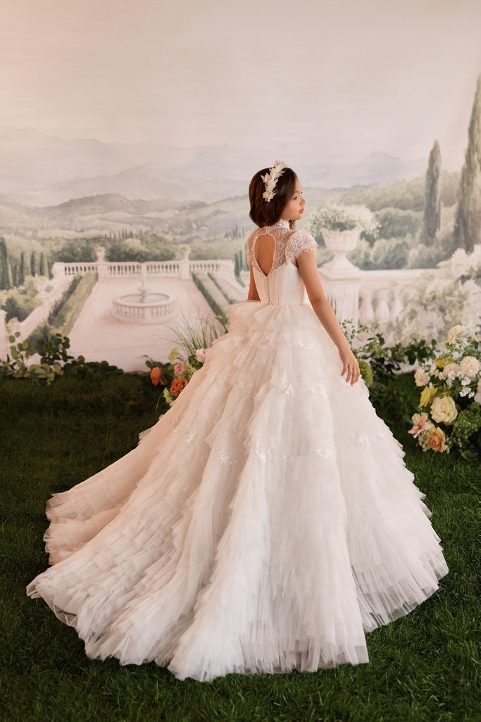 Girl wearing a white tiered tulle ball gown with lace bodice and floral headpiece standing on grass | Girls Formal Dress