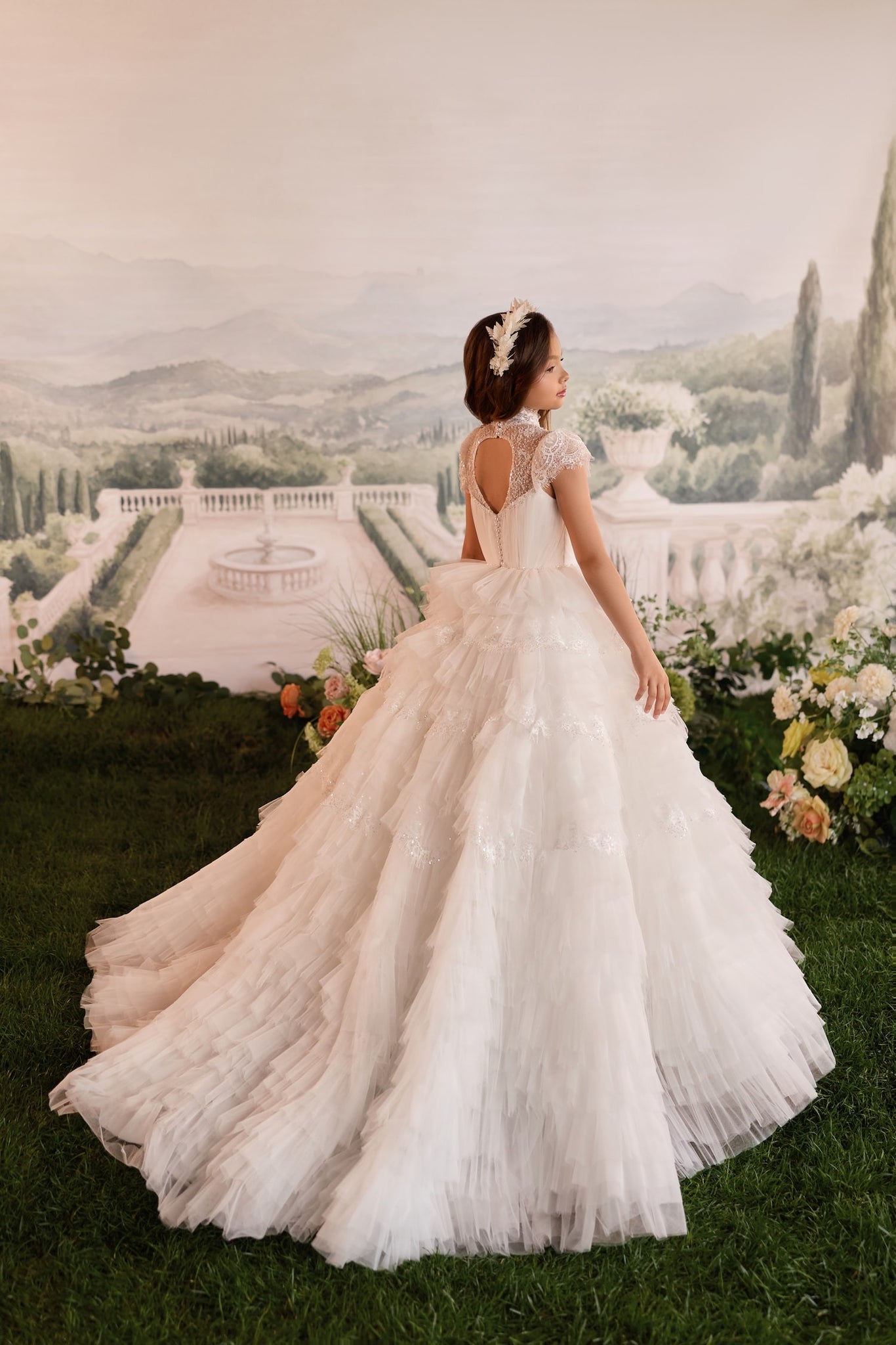 Girl wearing a white tiered tulle ball gown with lace bodice and floral headpiece standing on grass