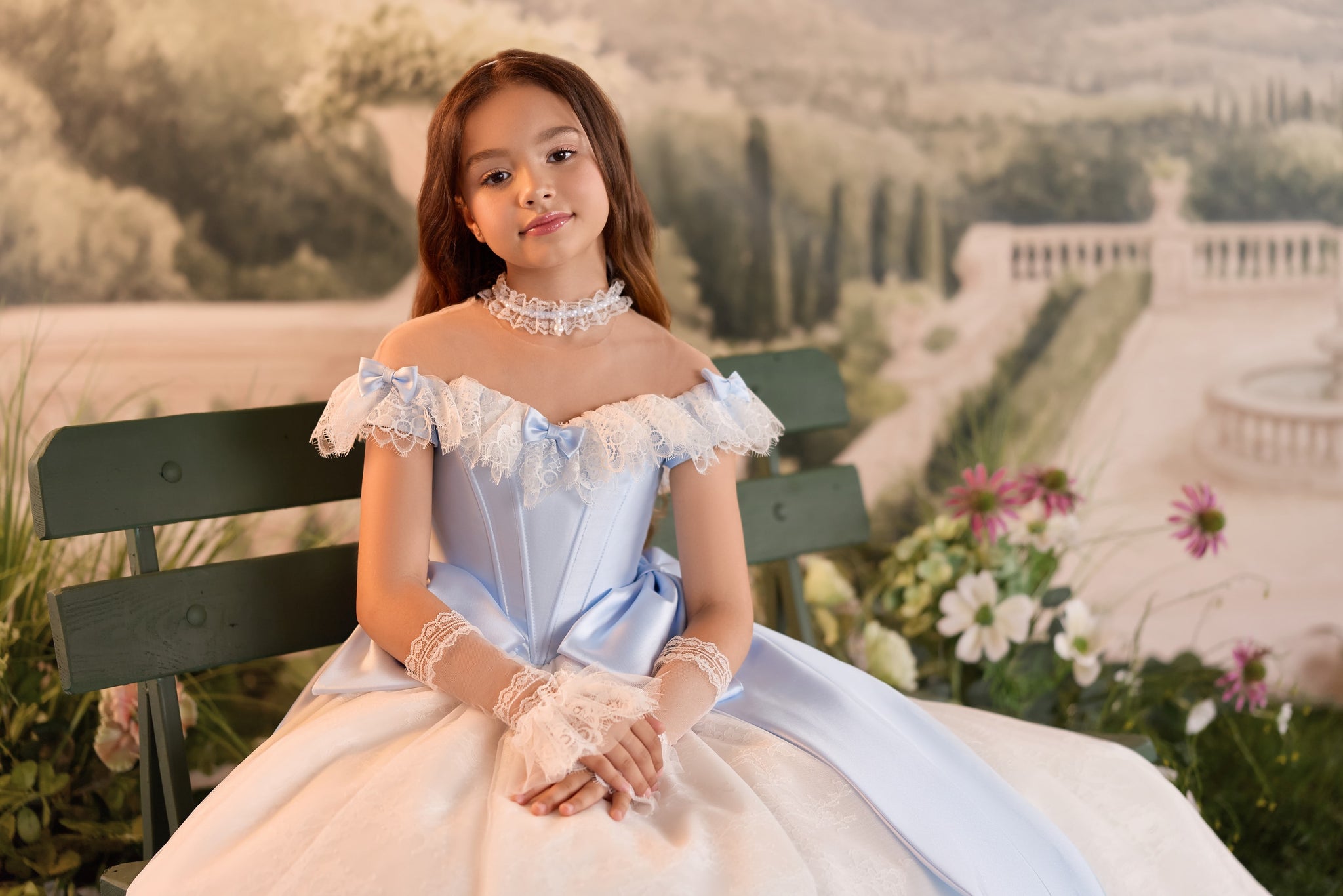 Girl wearing a light blue and white off-shoulder ball gown with lace gloves and a choker sitting on a garden bench