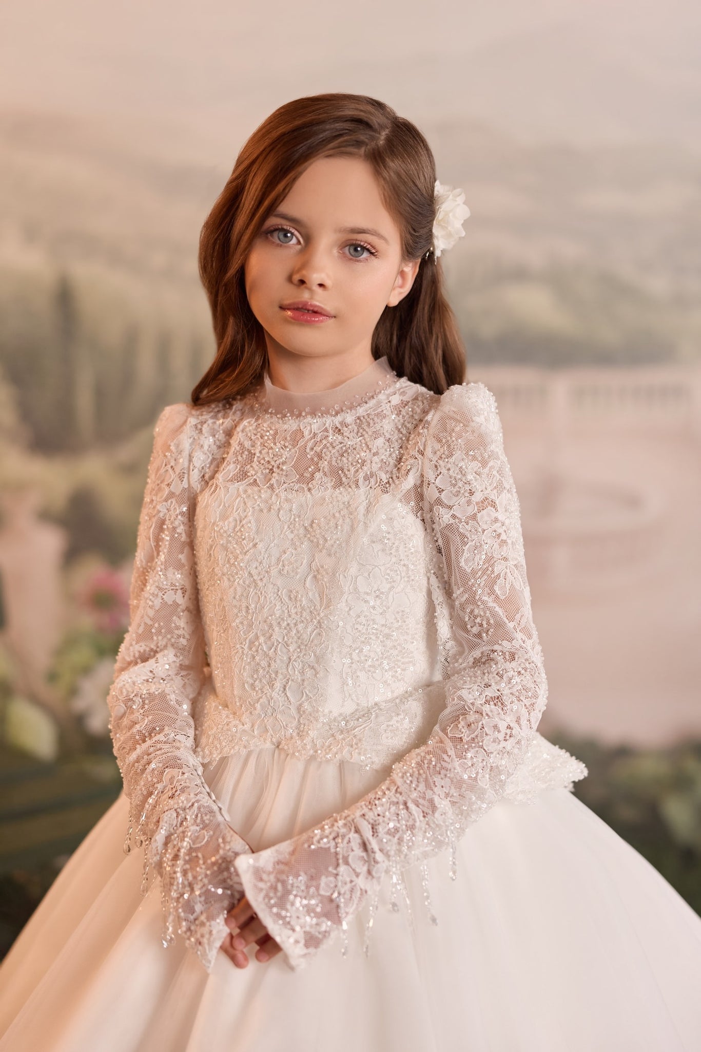 Girl wearing a white long sleeve lace dress with beaded details and a floral hair accessory