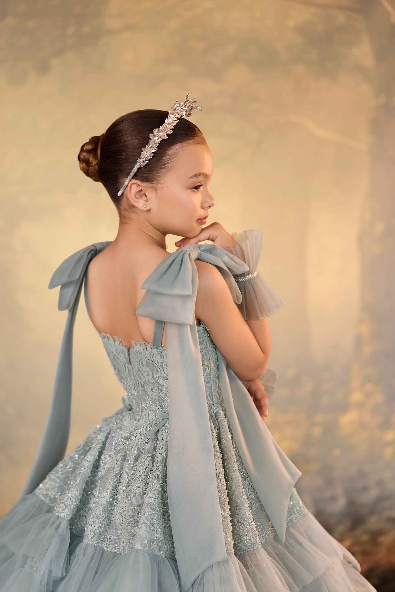 Girl wearing a sage green lace gown with bow shoulder straps and a crystal headband