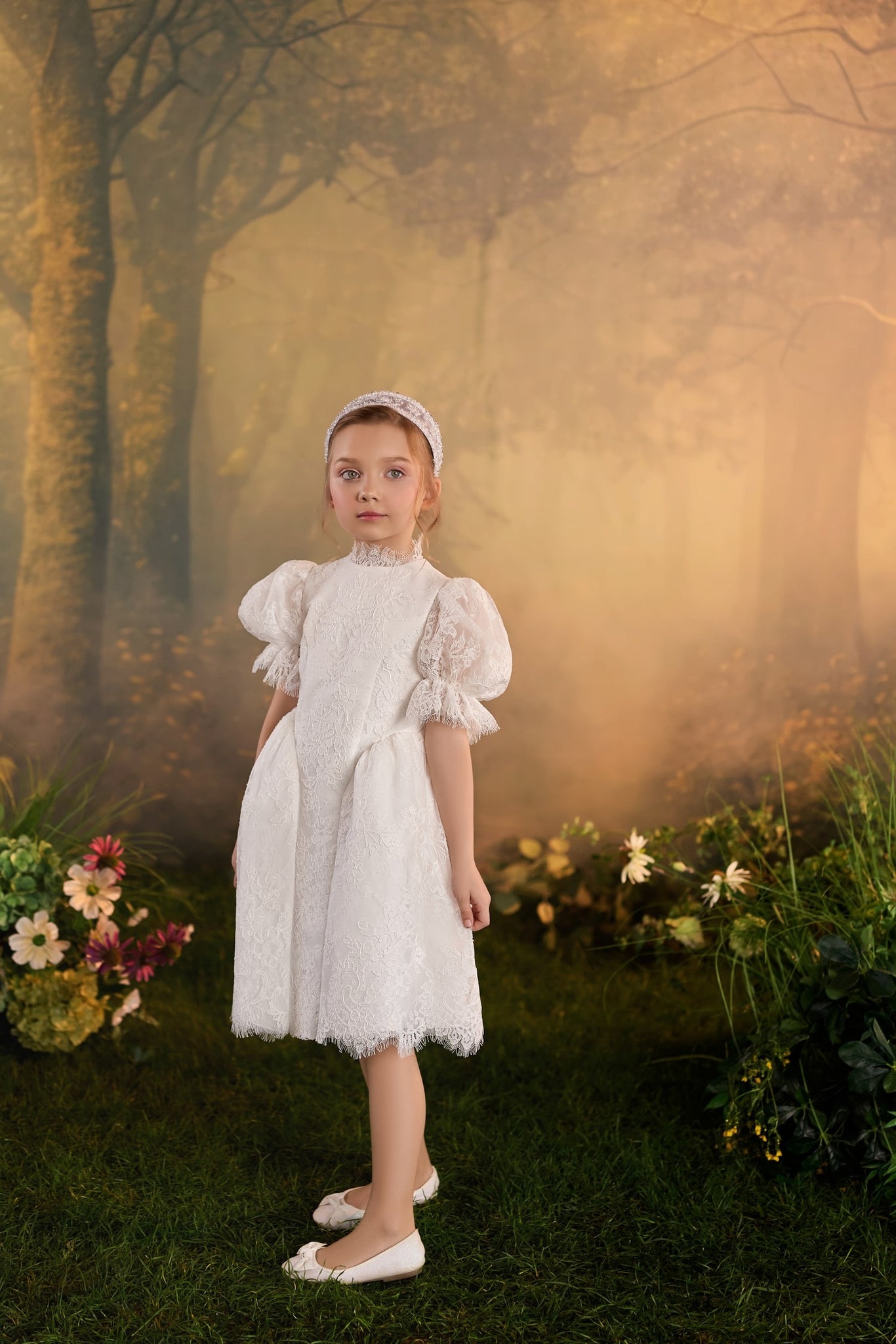 Girl wearing a white lace dress with puff sleeves and a headband standing in a forest setting | Girls Formal Dress