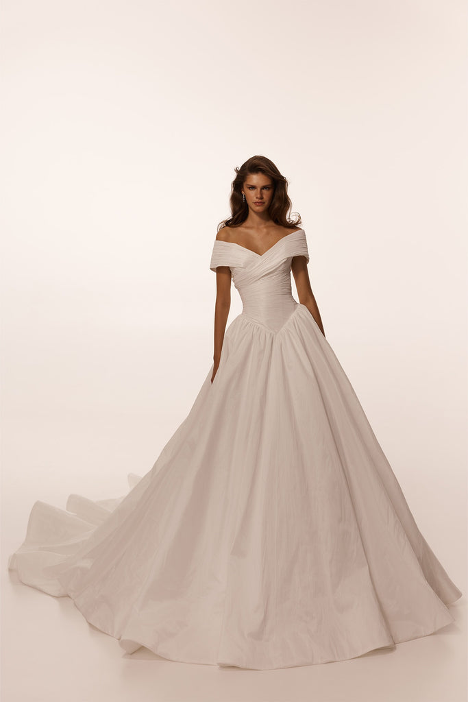 Model wearing a white off the shoulder ballgown wedding dress with a draped bodice and full skirt