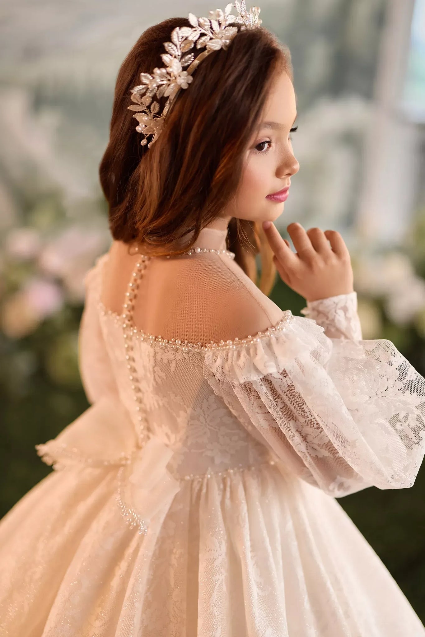 Girl wearing a white lace dress with pearl details and a floral headpiece
