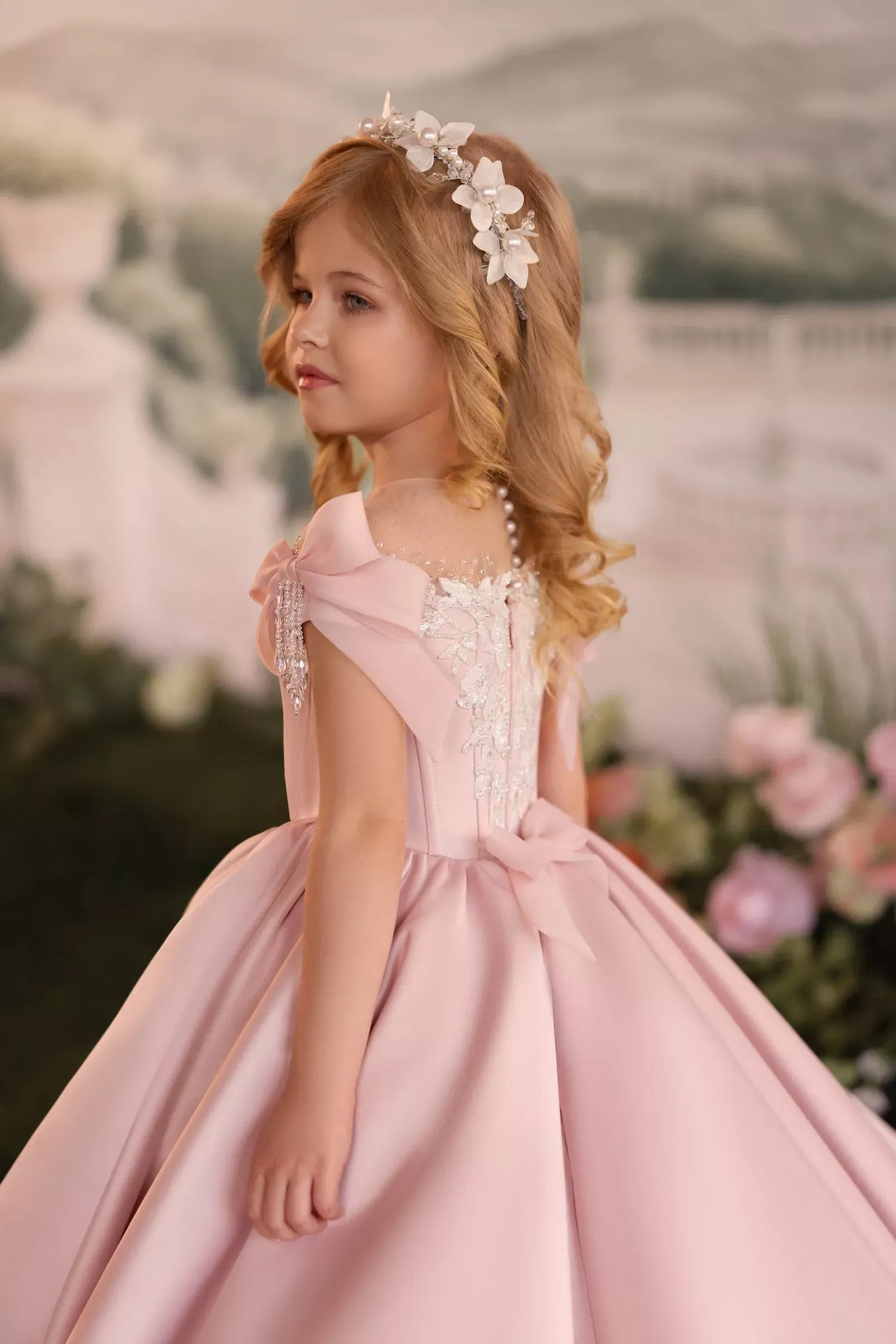 Girl wearing a pink satin ball gown with lace details and a floral headband