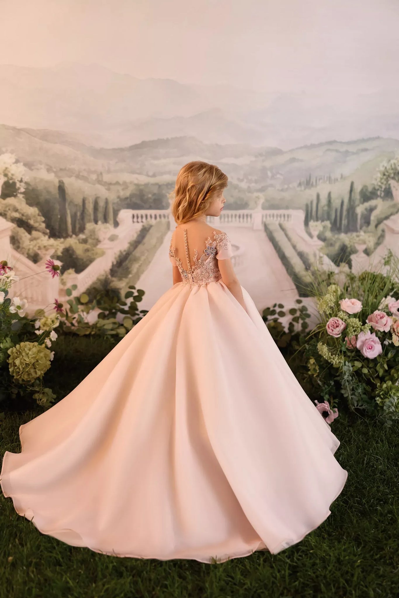 Girl wearing a pale pink floor length ball gown with lace detailing on the back