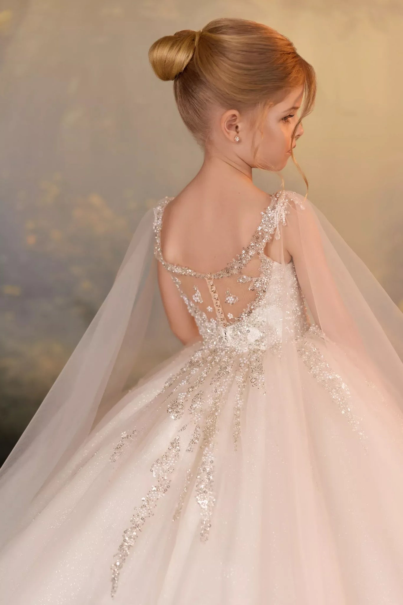 Girl wearing a white tulle ball gown with beaded bodice and sheer cape back