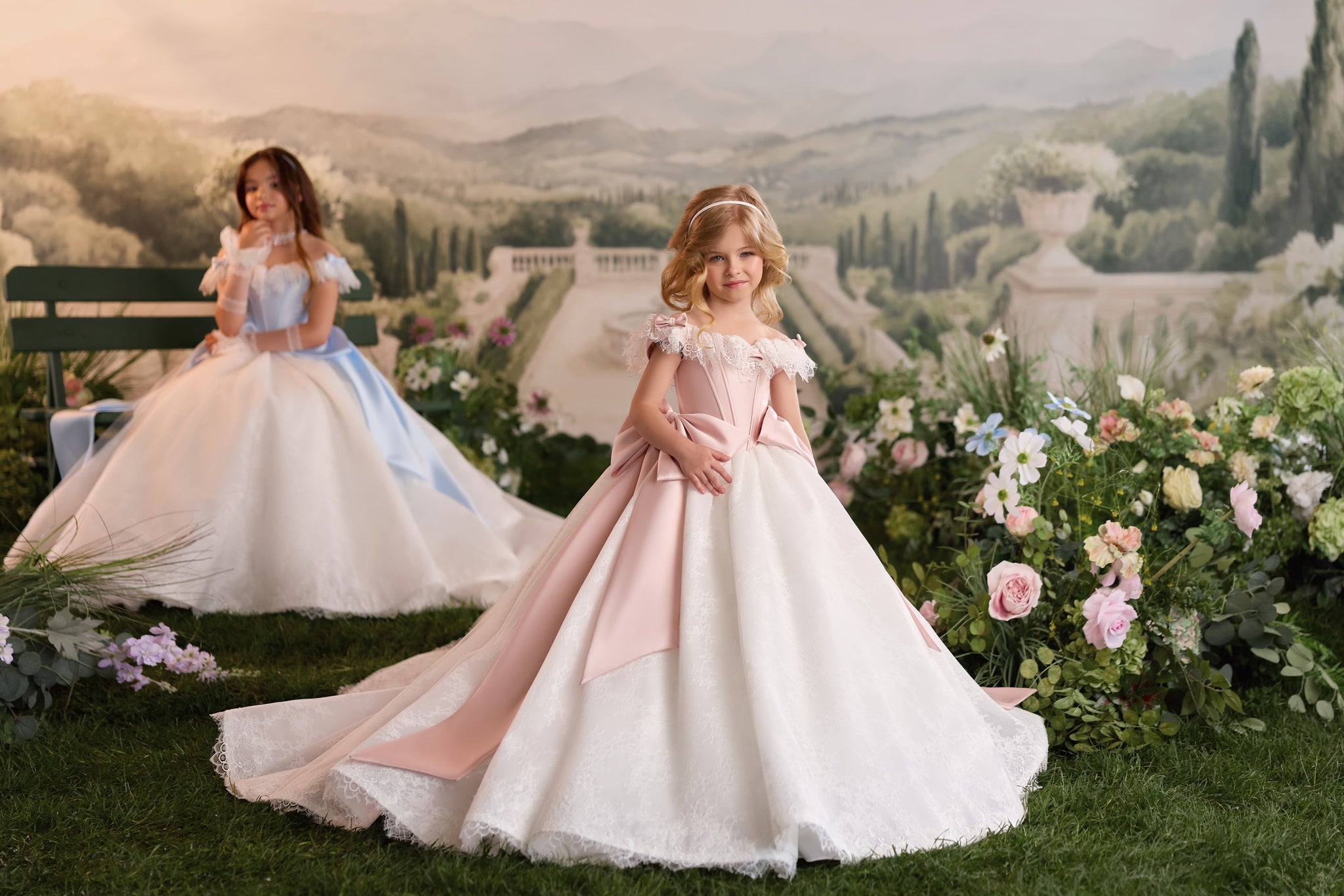 Two young girls wearing formal ball gowns in a garden setting