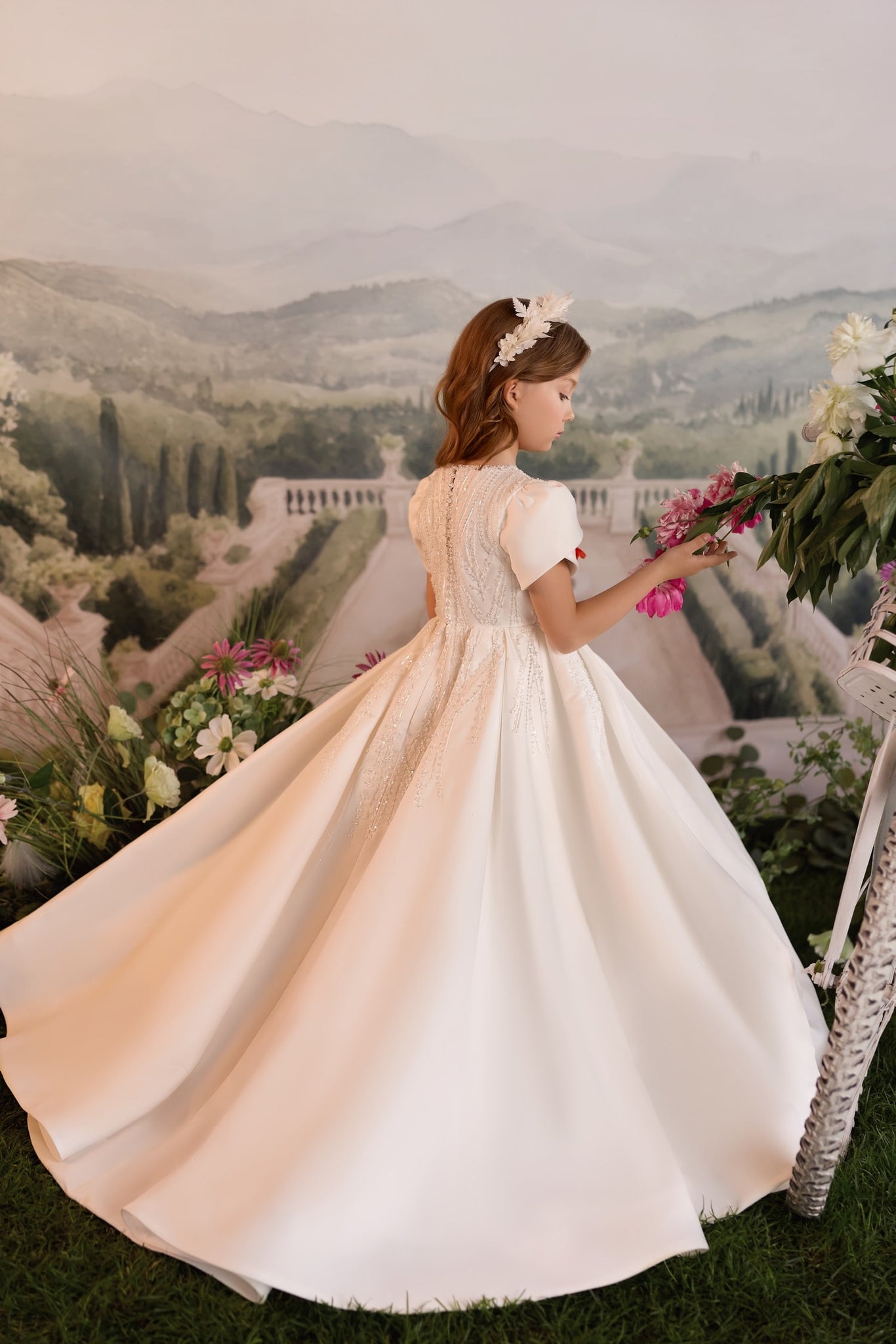 Girl wearing a white formal dress with beaded bodice and full skirt standing in a garden setting