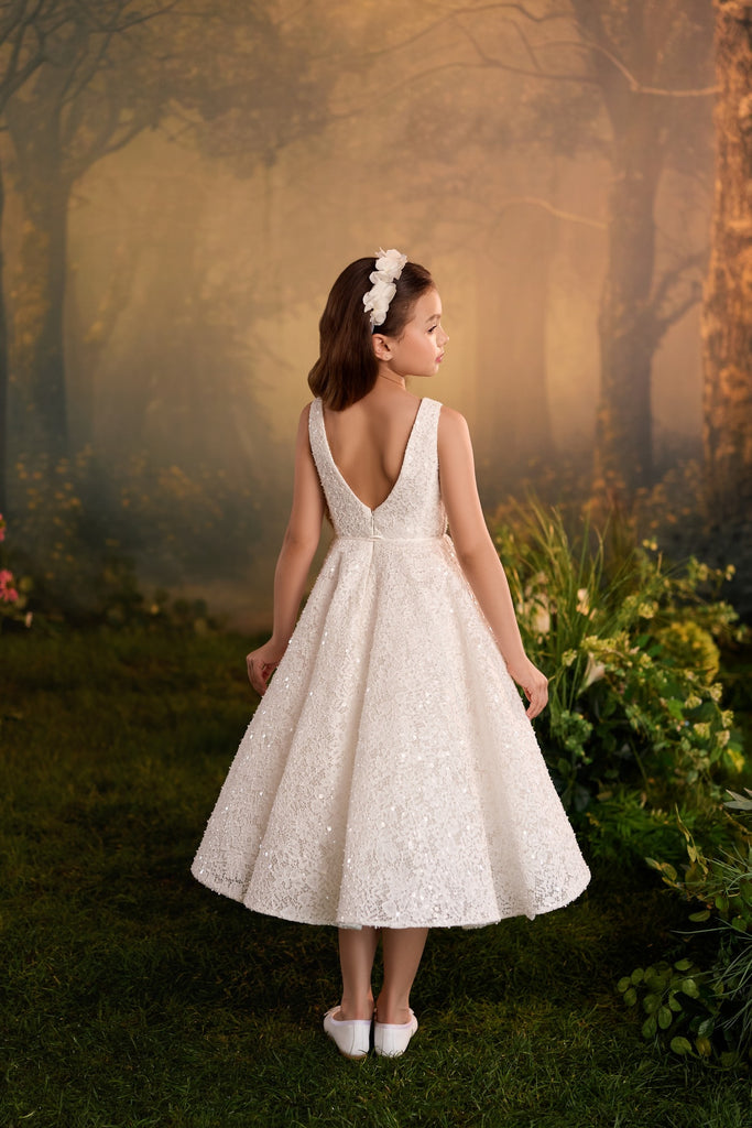 Girl wearing a white sequined A-line dress with a V-back and floral headband in a forest setting | Girls Formal Dress