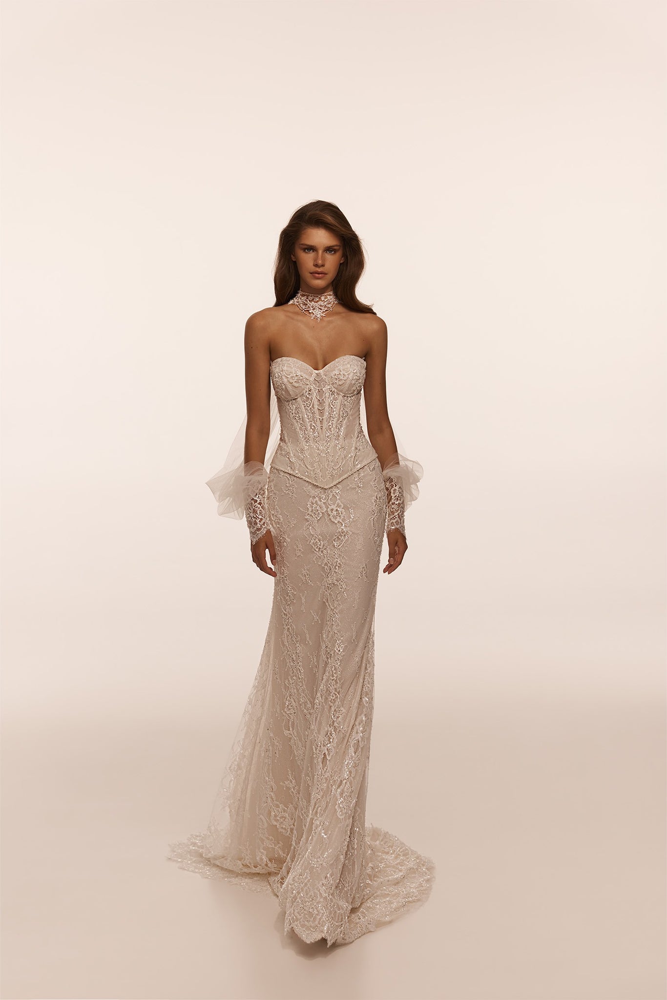 Model wearing a strapless lace corset wedding dress with sheer detachable sleeves and a lace choker