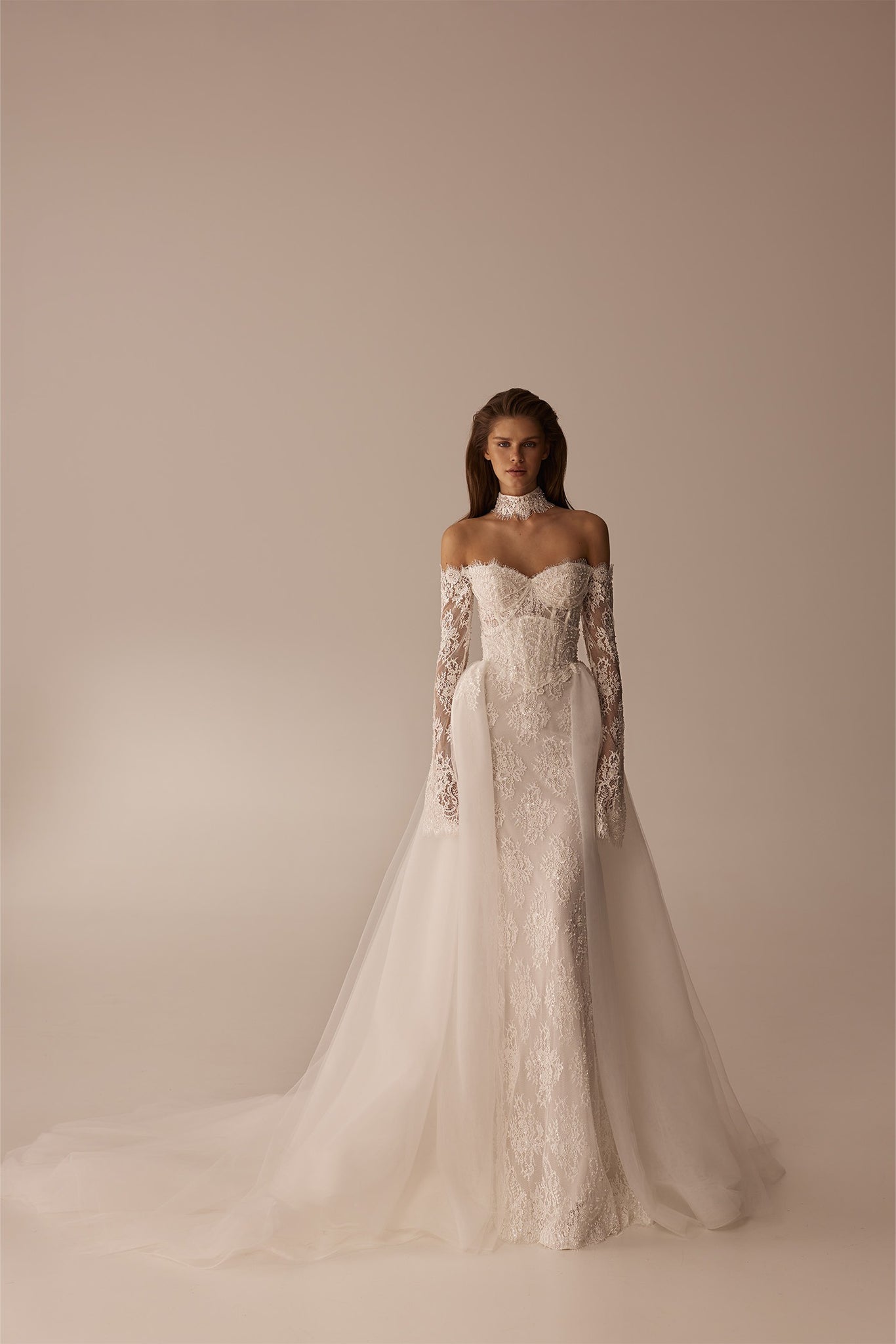 Model wearing an off the shoulder lace wedding dress with long sleeves and a tulle overskirt
