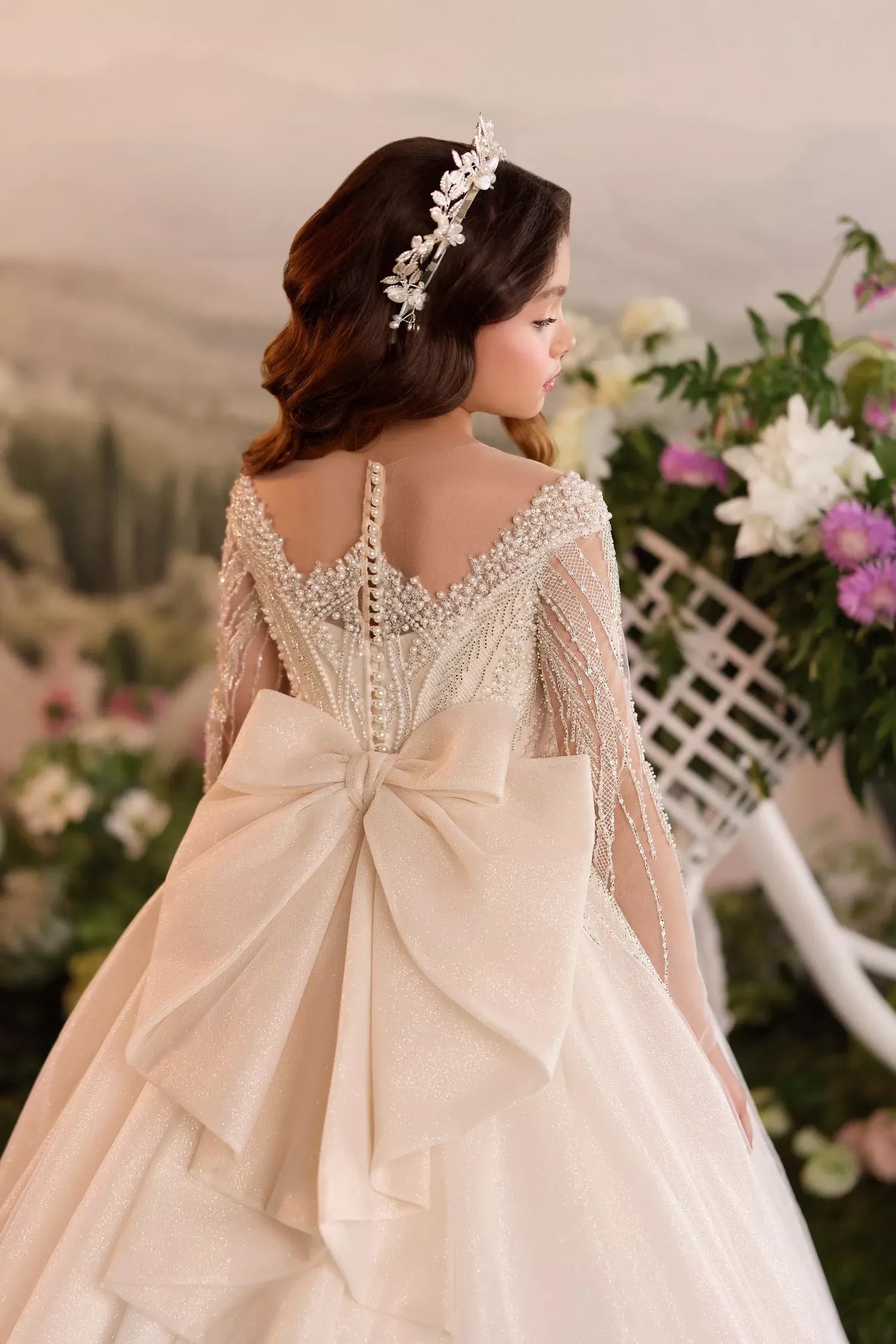 Girl wearing a beaded long sleeve gown with a large back bow and floral headpiece