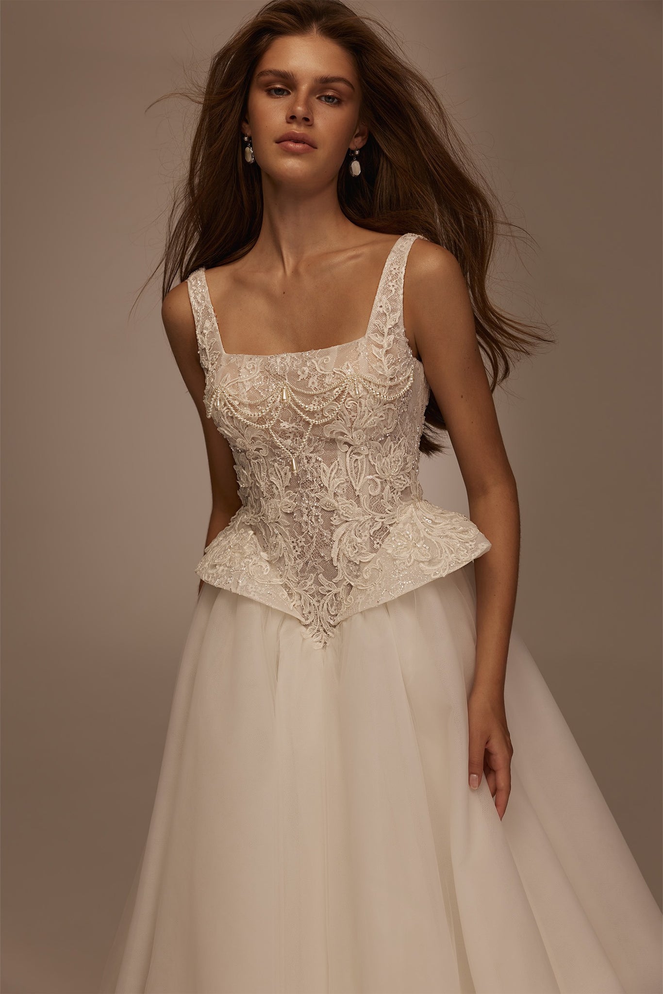 Model wearing a white lace corset wedding dress with pearl embellishments and a full tulle skirt