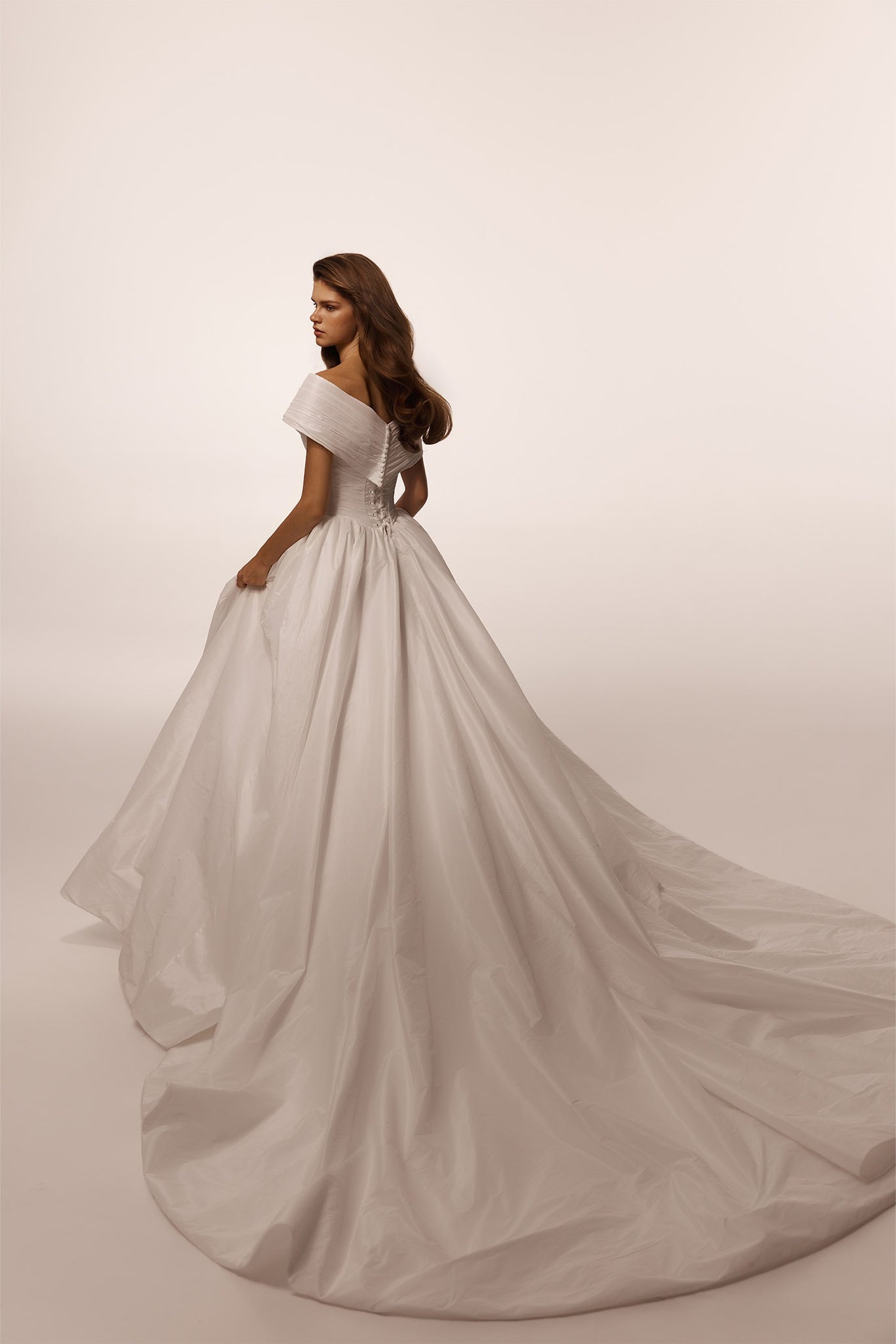 Woman wearing an off the shoulder white ballgown wedding dress with a long train