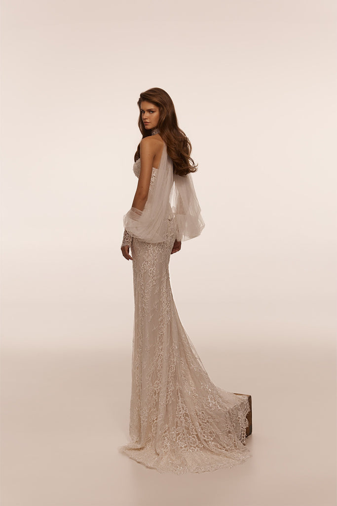 Model wearing a floor length lace wedding dress with sheer tulle sleeves and a high neckline
