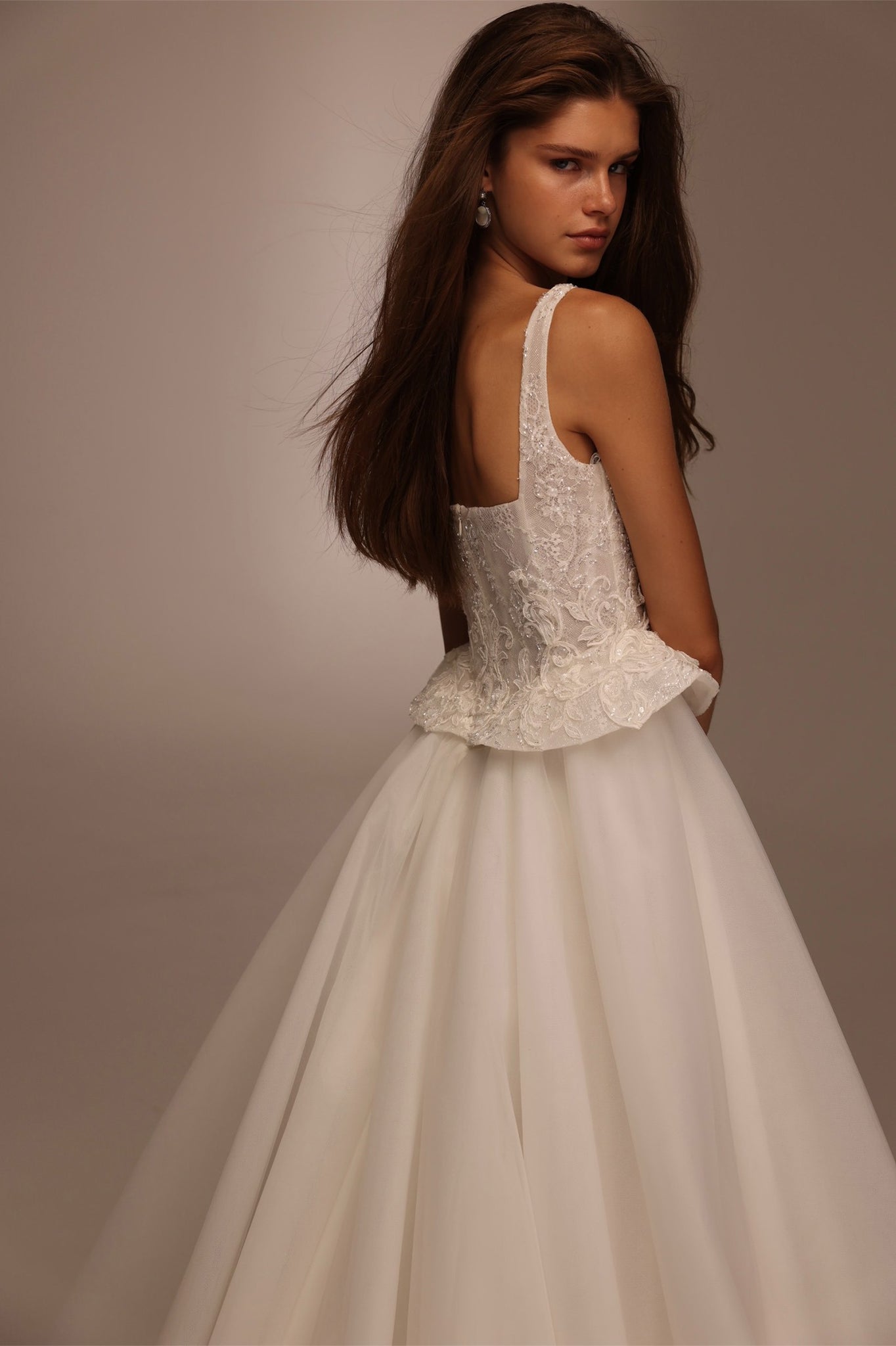 Woman wearing a white sleeveless wedding dress with a lace bodice and a peplum waist detail
