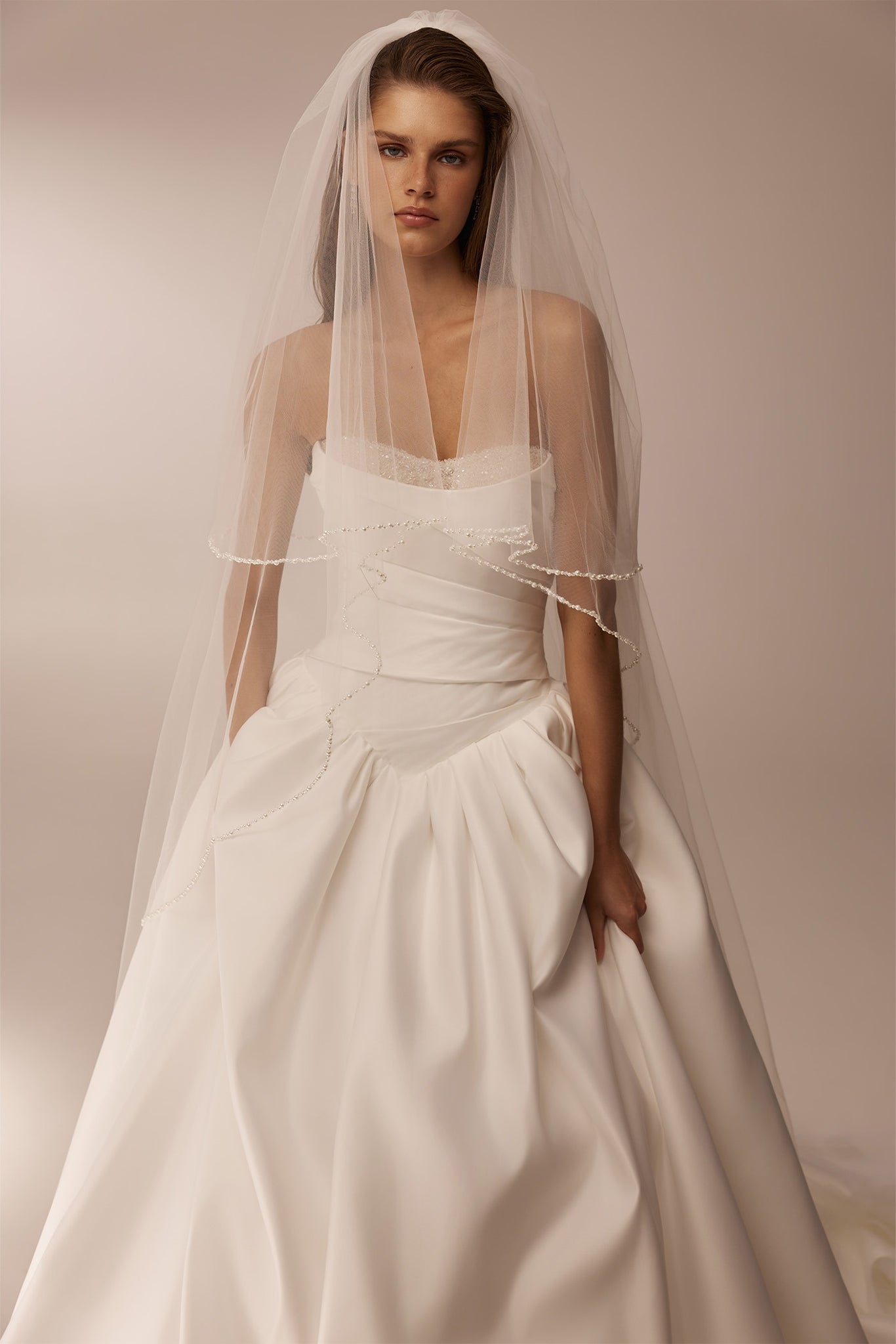 Model wearing a strapless white ballgown wedding dress and a sheer veil with beaded trim
