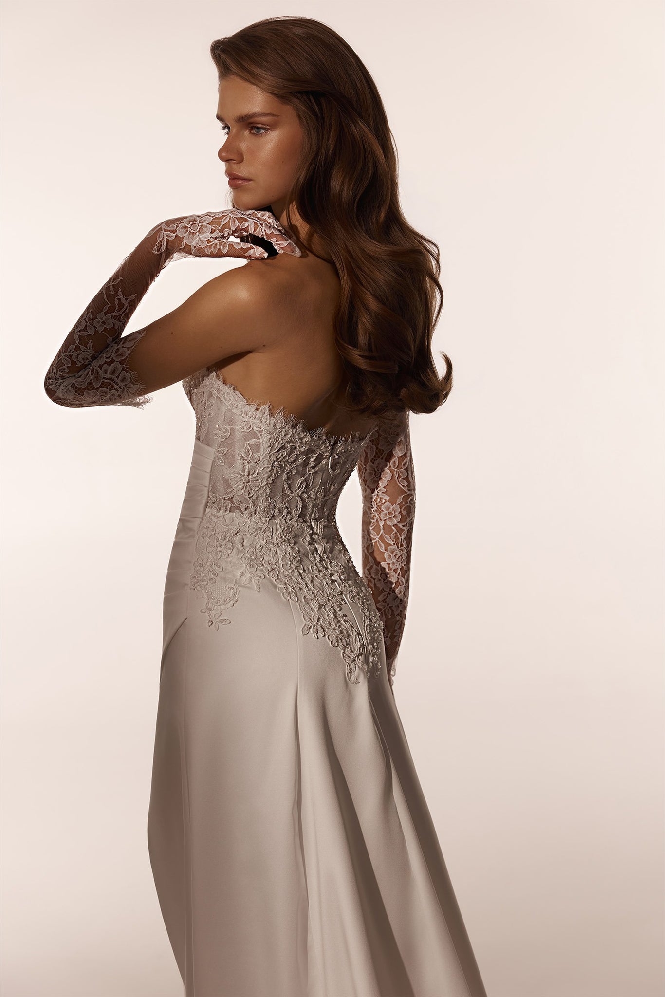 Woman wearing a strapless white wedding dress with lace sleeves and back detailing