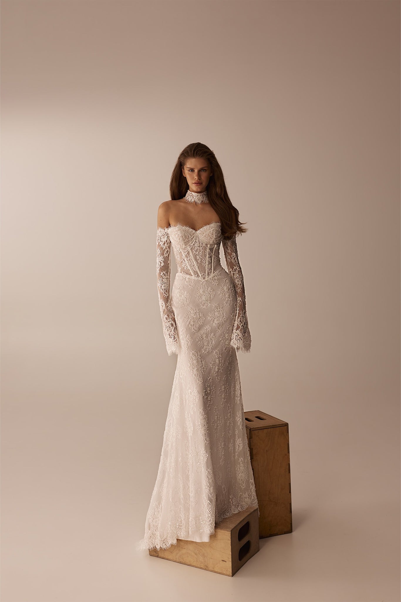 Model wearing a white lace off the shoulder wedding dress with long sleeves and a high neck choker
