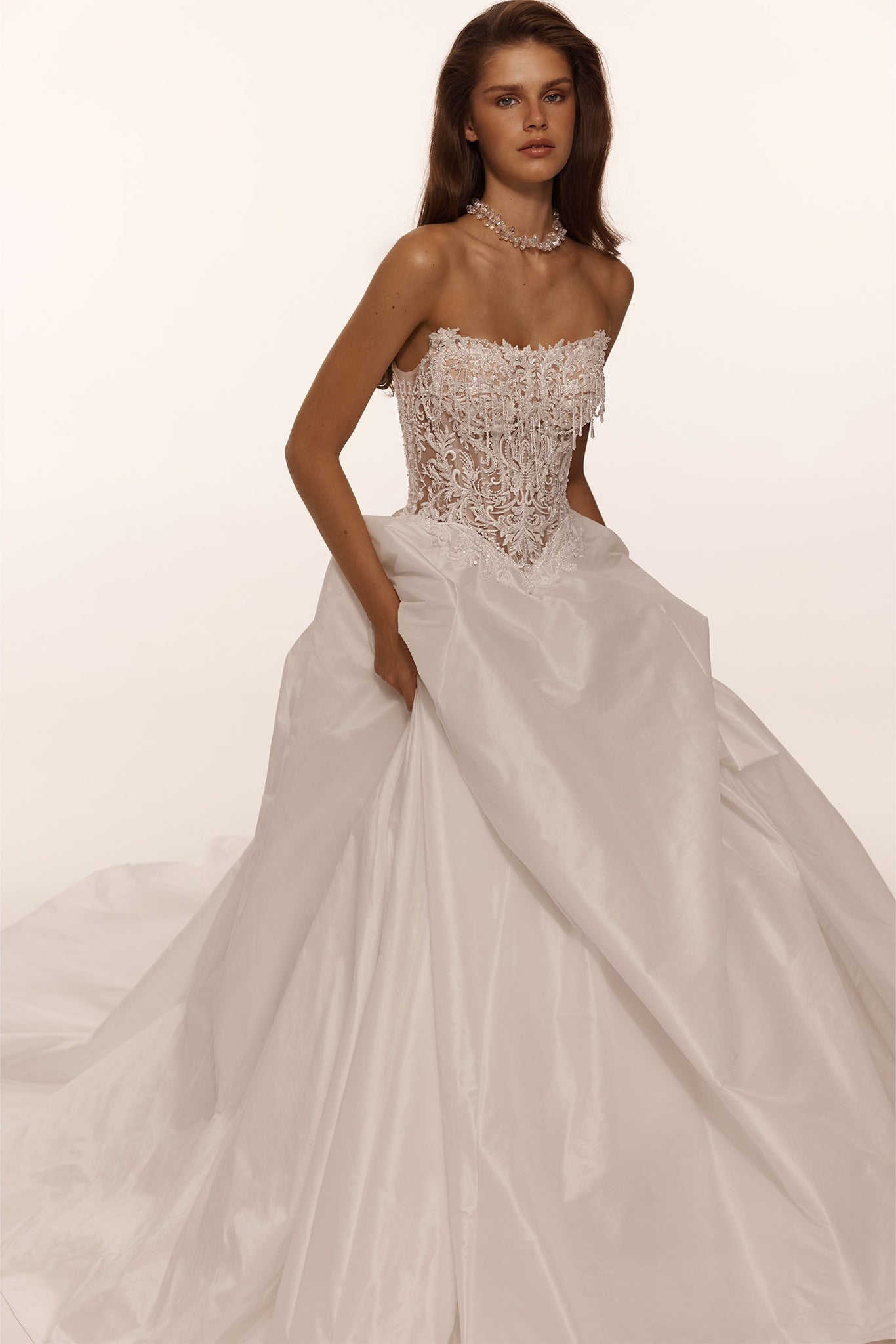 Model wearing a strapless white ballgown with a beaded lace corset bodice and full skirt