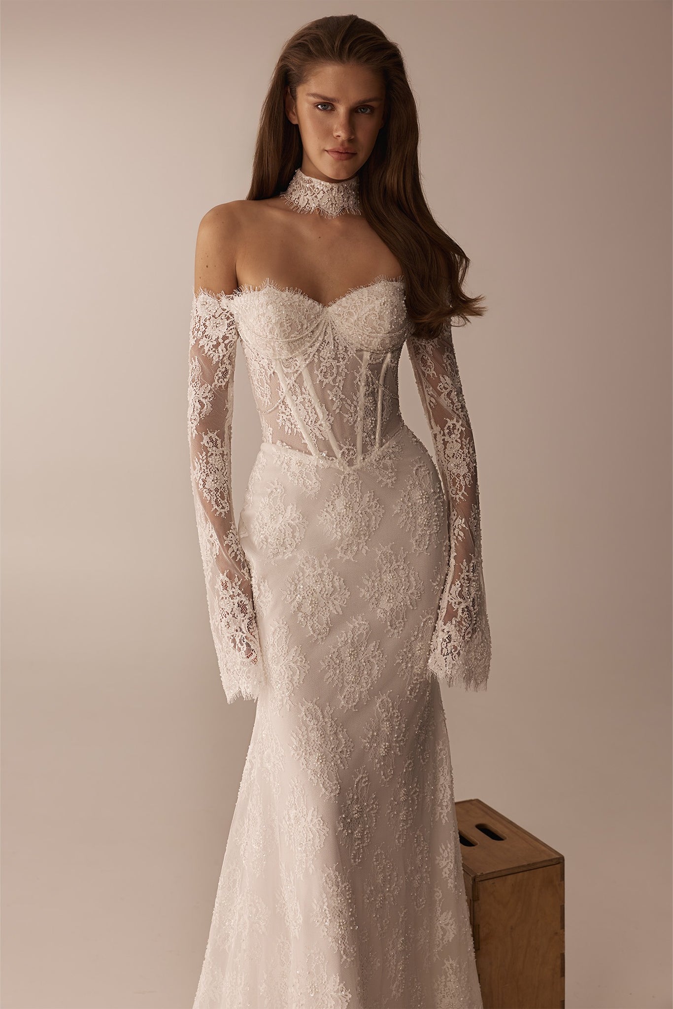 Model wearing a white lace off the shoulder wedding dress with long sleeves and a matching lace choker