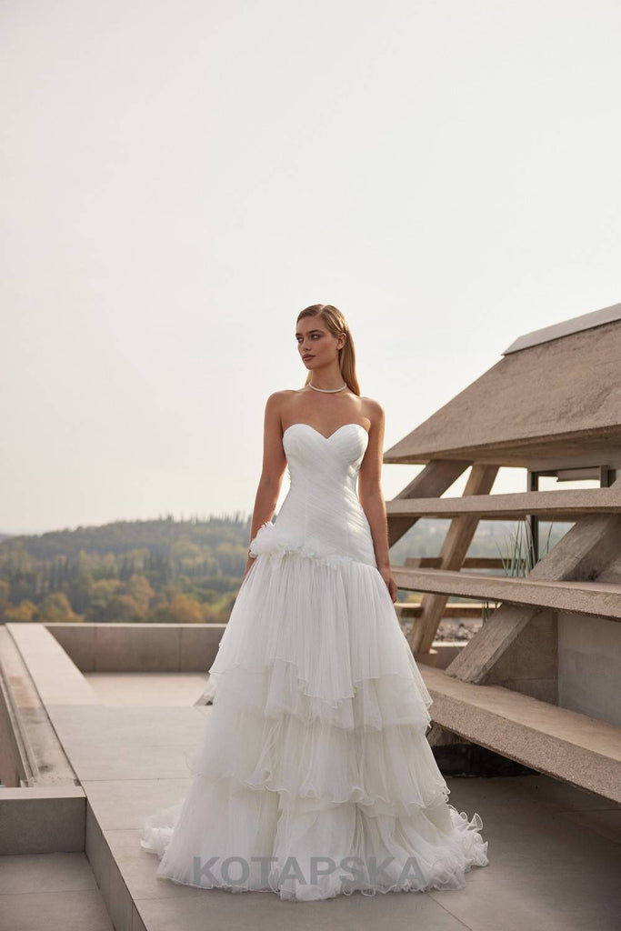 Strapless corset wedding dress with a structured bodice, layered pleated tulle skirt, and delicate organza floral appliqués at the waist