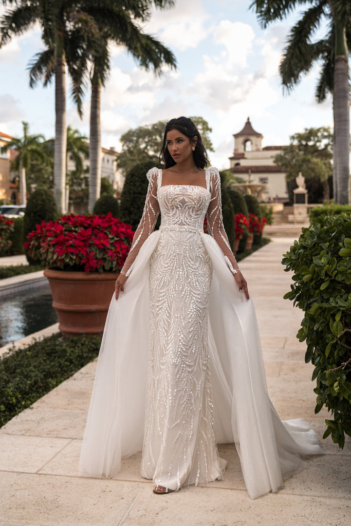 EMABRIDE 266 fitted wedding dress with square illusion neckline, long sleeves, allover embellishment, and detachable overskirt
