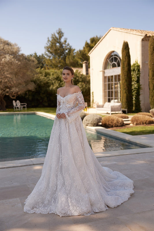 Woman wearing an off the shoulder lace wedding dress with long sleeves standing by a pool