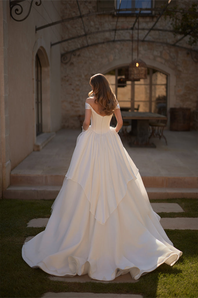 Back view of a woman wearing an off the shoulder ballgown wedding dress with a layered skirt
