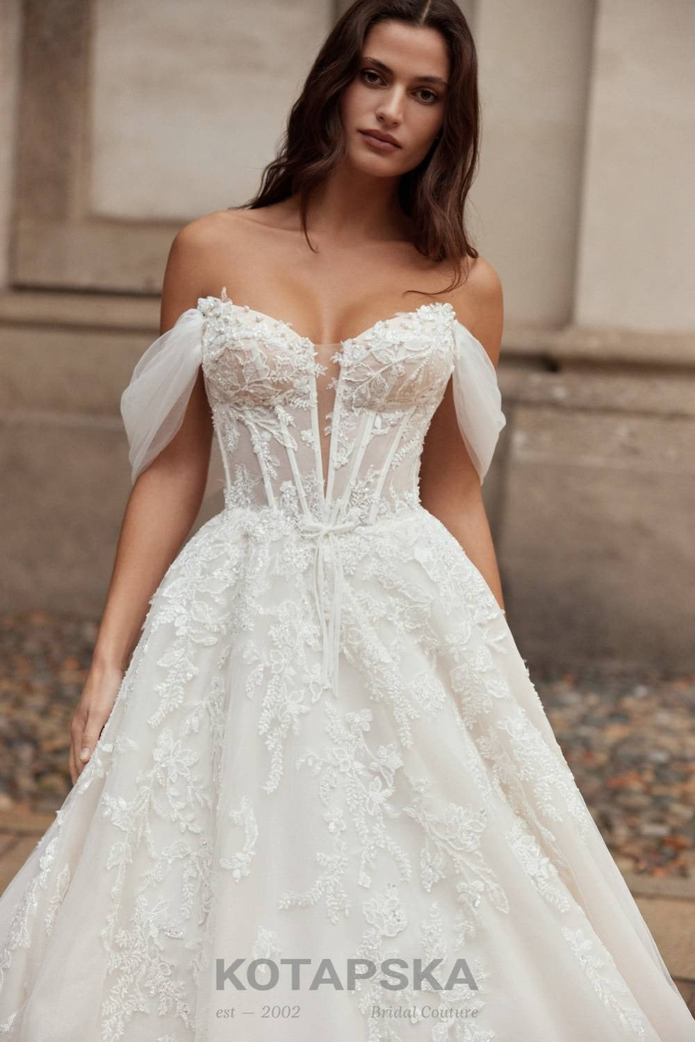 Close-up of a bridal gown with embroidered corset bodice, sheer detailing, and lace appliqués highlighting the neckline