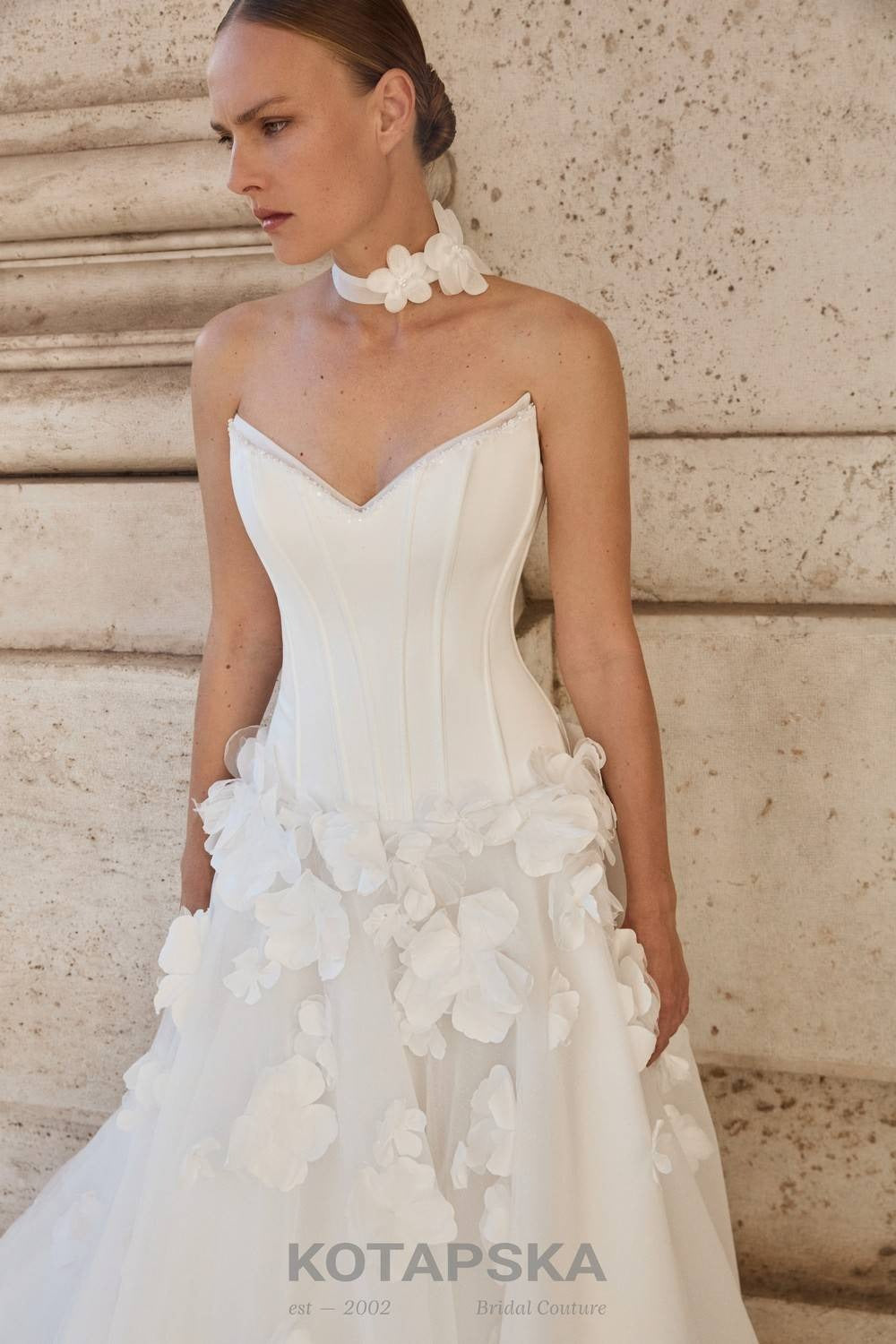 Strapless corset wedding dress with a structured minimalist bodice and voluminous A-line skirt featuring delicate 3D floral appliqués and a soft flowing train