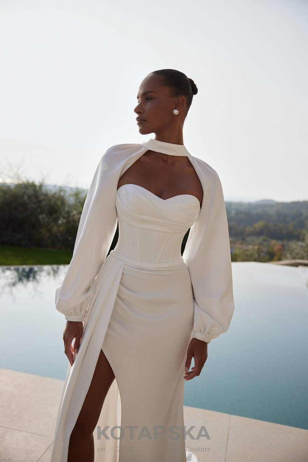 Strapless satin corset wedding dress with a fitted silhouette, high slit, lace-up back, and detachable long sleeves for a modern elegant look