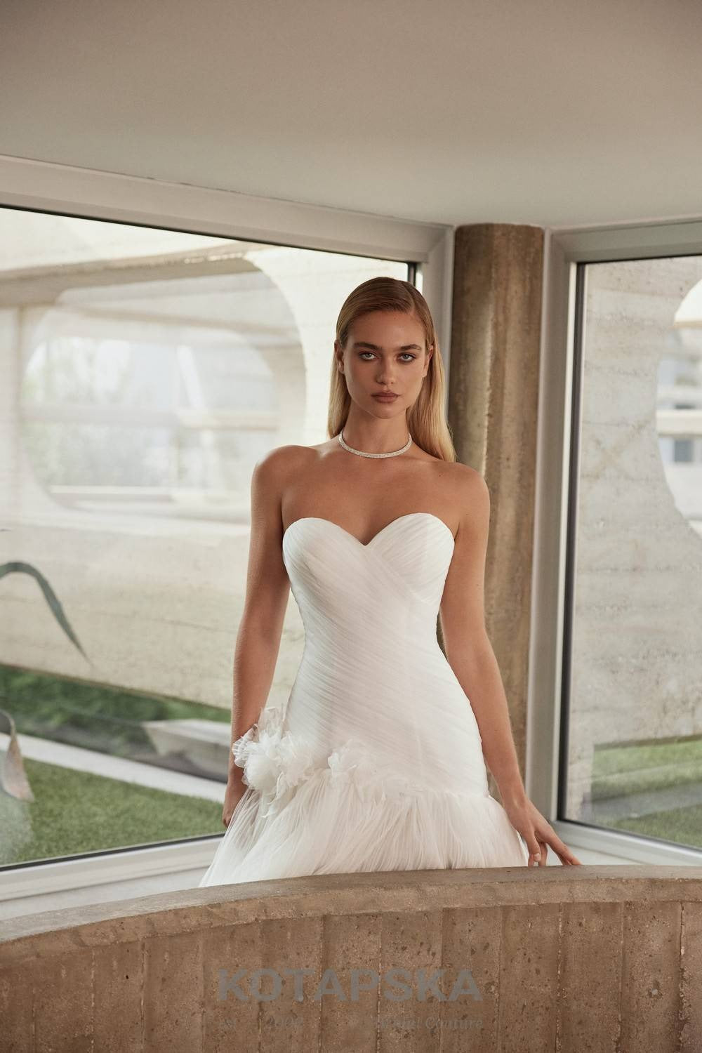 Strapless corset wedding dress with a structured bodice, layered pleated tulle skirt, and delicate organza floral appliqués at the waist