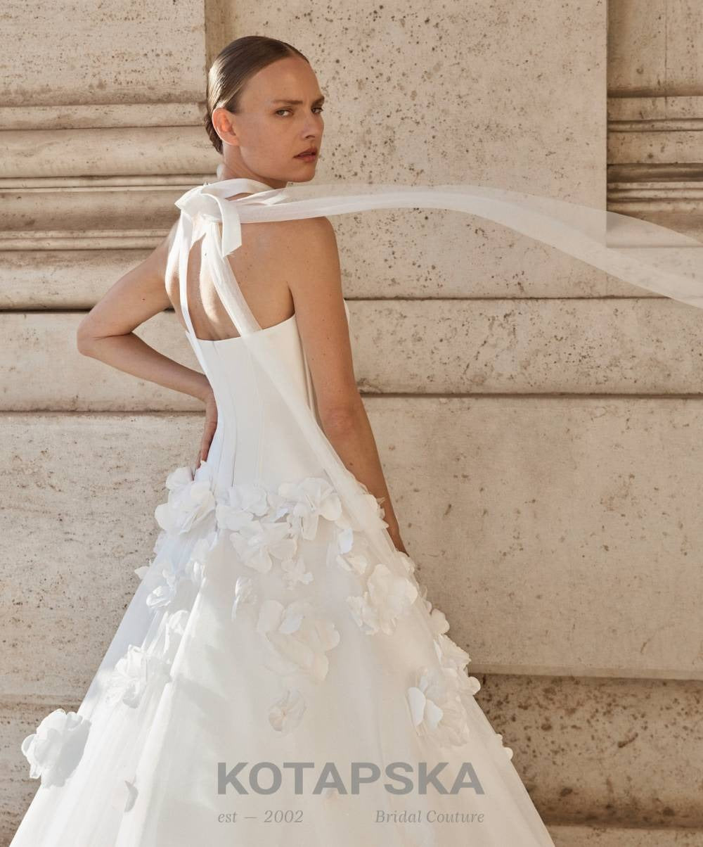 Strapless corset wedding dress with a structured minimalist bodice and voluminous A-line skirt featuring delicate 3D floral appliqués and a soft flowing train