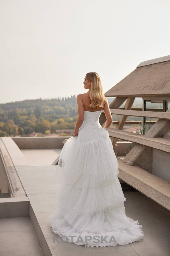 Strapless corset wedding dress with a structured bodice, layered pleated tulle skirt, and delicate organza floral appliqués at the waist