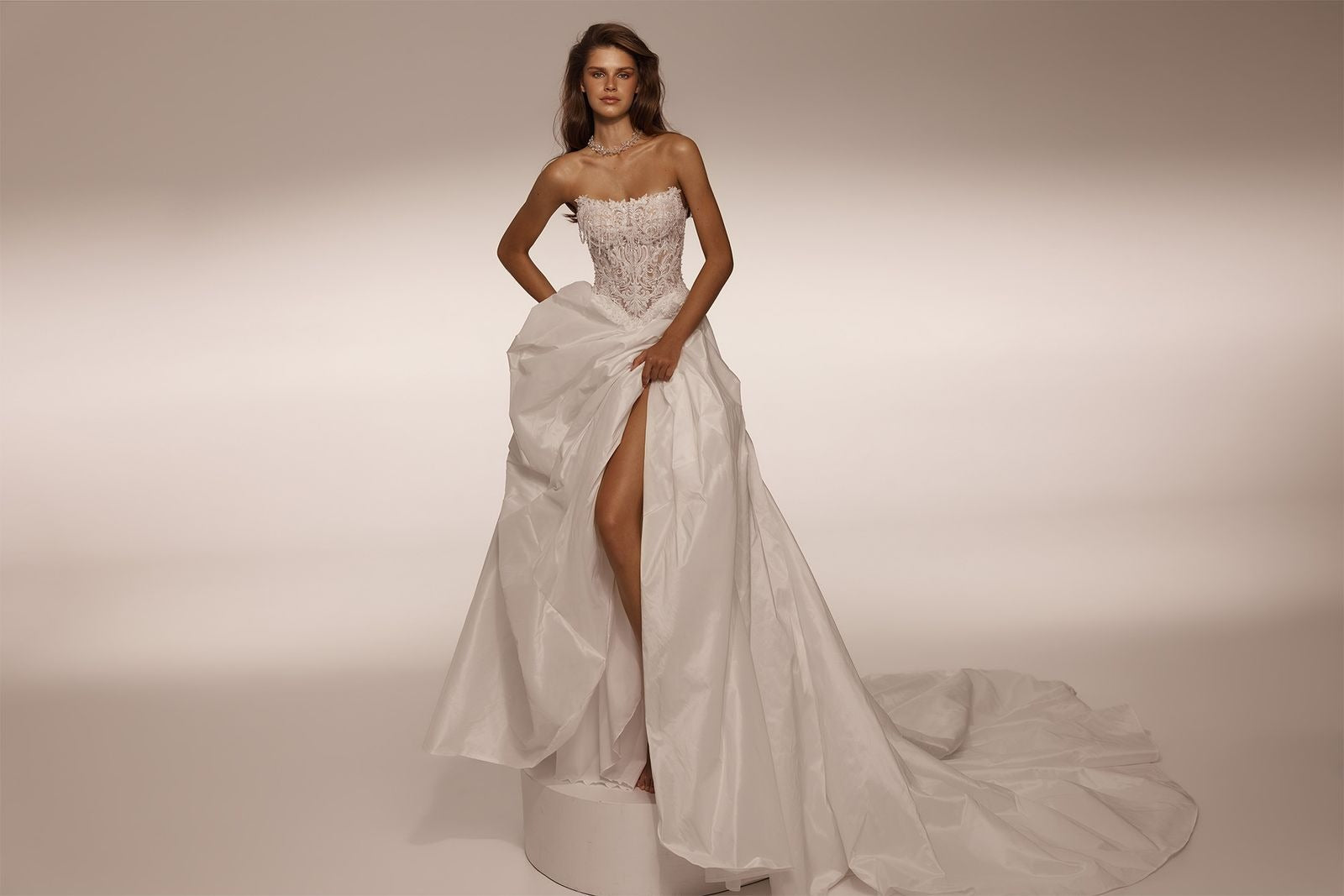 Model wearing a strapless lace bodice wedding dress with a high slit and full skirt