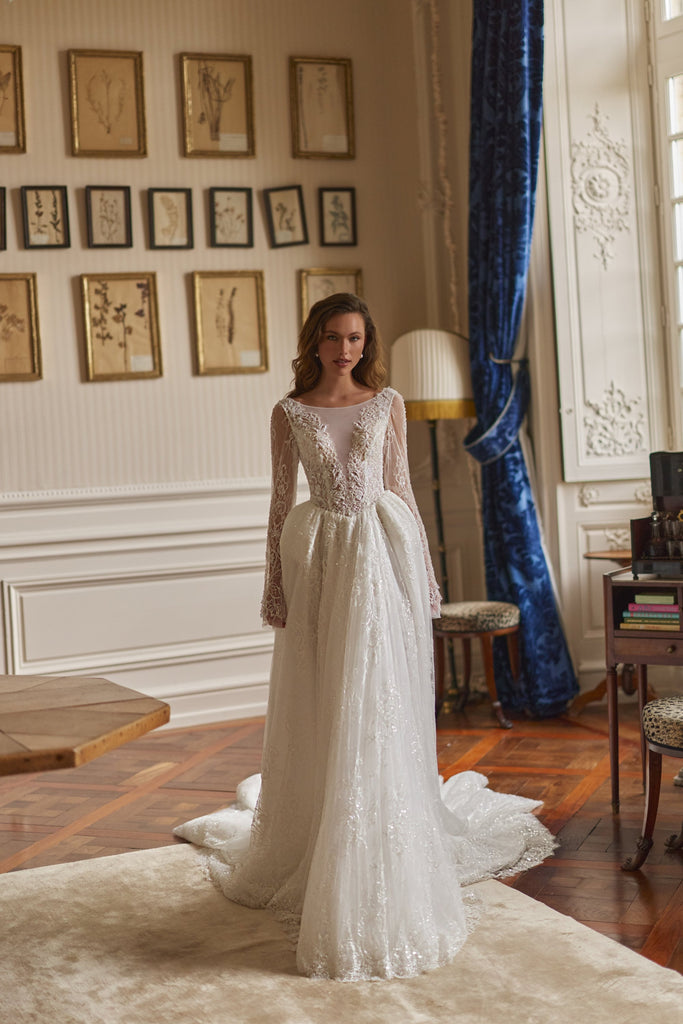 Woman wearing a long sleeve lace wedding dress with a full skirt in a room with framed botanical prints
