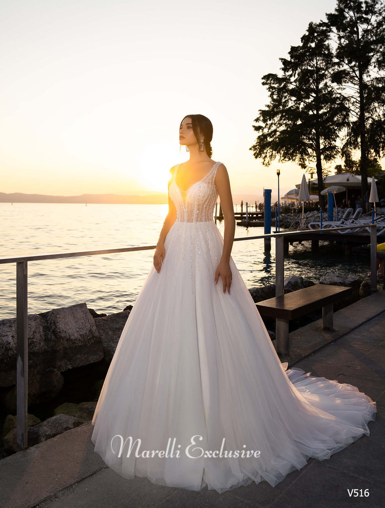 Woman wearing a white sleeveless A-line wedding dress with beaded bodice standing by a lake at sunset